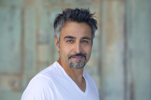 Nicholas Guilak — white V-neck t-shirt against a soft green-gray textured backdrop